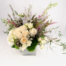 Cream roses and white blossoms in a square glass vase