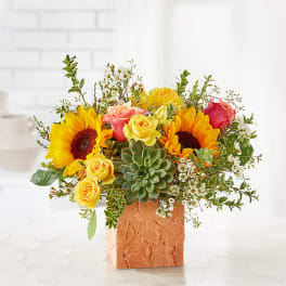 Sunflowers and roses arranged with a succulent in a textured square vase