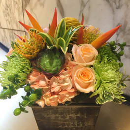 Tropical floral arrangement in a square planter with roses and succulents