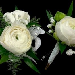 Two white floral boutonnieres with ribbon and pearl accents on a black background