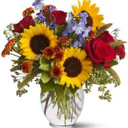 Bouquet of sunflowers, red roses, and blue flowers in a glass vase