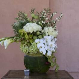White floral arrangement in a green glass vase with calla lilies and orchids