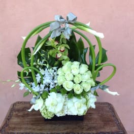 White floral arrangement with green loops and gray ribbon on a black base