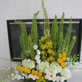 Tall floral arrangement with yellow orchids, white roses, and green spikes in a black container