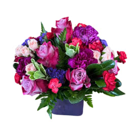 Mixed pink, purple, and red flower arrangement in a purple vase