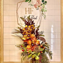 Tall floral arrangement in a glass vase with orange and burgundy blooms
