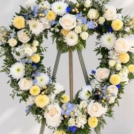Heart-shaped floral wreath with white, yellow, and blue flowers on an easel