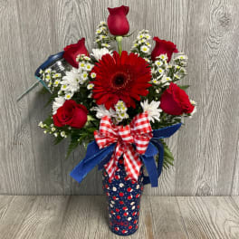 Red roses and daisies arranged in a patterned tumbler with a ribbon bow