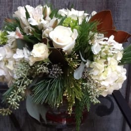 White floral arrangement in a glass vase with pine accents