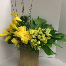 Yellow calla lilies and roses in a gold rectangular vase