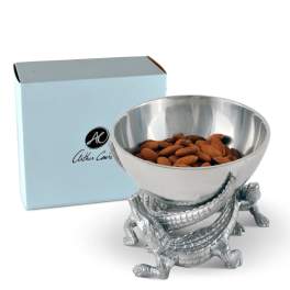 Silver bowl on a crocodile stand filled with almonds, with a light blue box behind it.