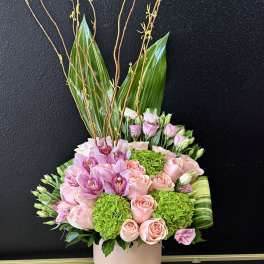 Pink roses and orchids in a pale pink vase with tall branches