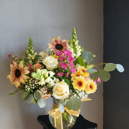 Mixed bouquet in a glass vase with roses, sunflowers, and pink filler flowers