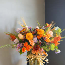 Orange and lavender mixed bouquet in a glass vase with raffia bow