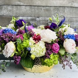 Low floral arrangement in a gold bowl with white, purple, pink, and blue blooms