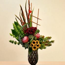 Tall mixed floral arrangement in a dark vase with red, yellow, and green blooms