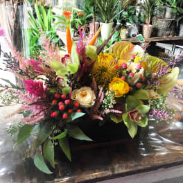 Mixed floral arrangement with orchids, roses, and bright tropical blooms in a dark container