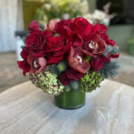 Red roses and burgundy orchids arranged in a green glass vase
