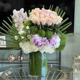 Large pastel floral arrangement in a glass vase with roses, orchids, and hydrangeas