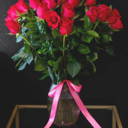 Bouquet of red roses in a ribbed glass vase with a pink ribbon