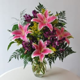 Pink lilies and purple flowers in a clear glass vase