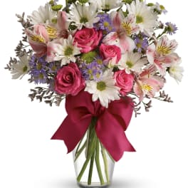 Bouquet of pink roses, white daisies, and alstroemeria in a glass vase with a ribbon