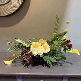 Low floral arrangement with yellow calla lilies and burgundy blooms in a black bowl