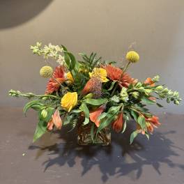 Mixed orange and yellow floral arrangement in a square glass vase