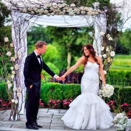 Bride and groom under a floral wedding arch with white roses