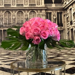 Pink rose bouquet in a clear glass vase with large tropical leaves