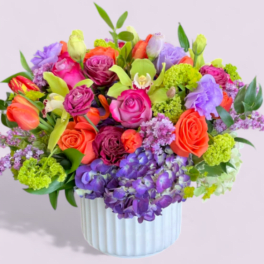 Bright mixed arrangement of orange, pink, and purple flowers in a white ceramic vase