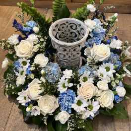 Circular floral wreath with white and blue flowers around a decorative stone urn