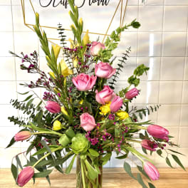 Tall mixed bouquet with pink roses, pink tulips, and yellow blooms in a glass vase