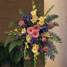 Tall standing spray with pink gerbera daisies, yellow blooms and purple irises in a fan-shaped design