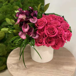 Hot pink roses and purple calla lilies in a white cylinder vase on a wooden table