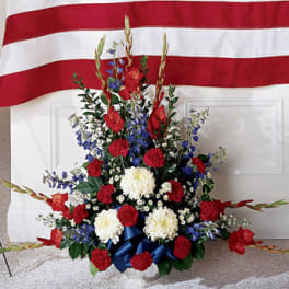 Red, white, and blue floral standing spray in front of a flag