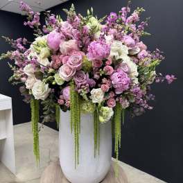 Tall arrangement of pink and white roses and peonies with trailing green accents in a white vase