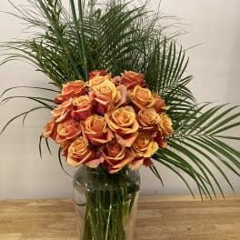 Orange roses arranged in a clear glass vase with tall palm fronds