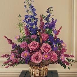 Tall basket arrangement of pink roses, purple irises, and lavender asters in a woven wicker basket