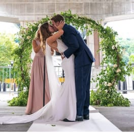 Bride and groom kissing under a greenery-covered wedding arch