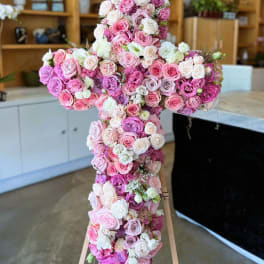 Large cross-shaped floral arrangement of pink and white roses on a stand
