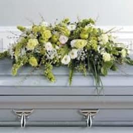 Long white and green flower casket spray arranged on top of a light gray casket.