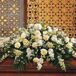 Large white and cream floral casket spray arranged in a low, elongated shape