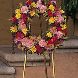 Standing wreath of mixed pink, yellow, red, and purple flowers on a gold easel.