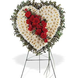 Heart-shaped white floral wreath with red flowers on a metal easel stand