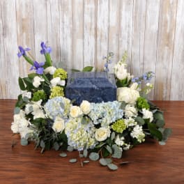 Low white and blue floral arrangement surrounding a square blue urn