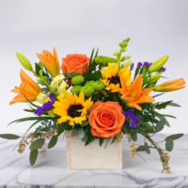 Orange roses and sunflowers in a wooden box with purple accents