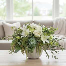 Low white lily and rose arrangement with succulents in a gray pot on a coffee table