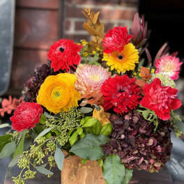 Bright mixed bouquet with red, yellow, and pink blooms in a wooden container
