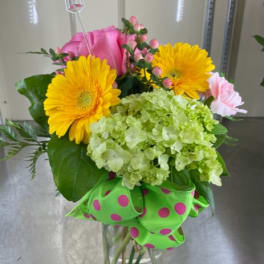 Bouquet of yellow gerbera daisies, pink roses, and green hydrangea in a glass vase